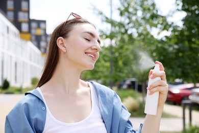 Photo of Smiling woman spraying thermal water onto her face outdoors