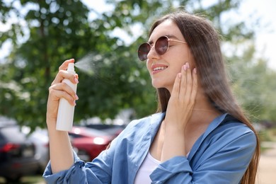 Photo of Smiling woman in sunglasses spraying thermal water onto her face outdoors
