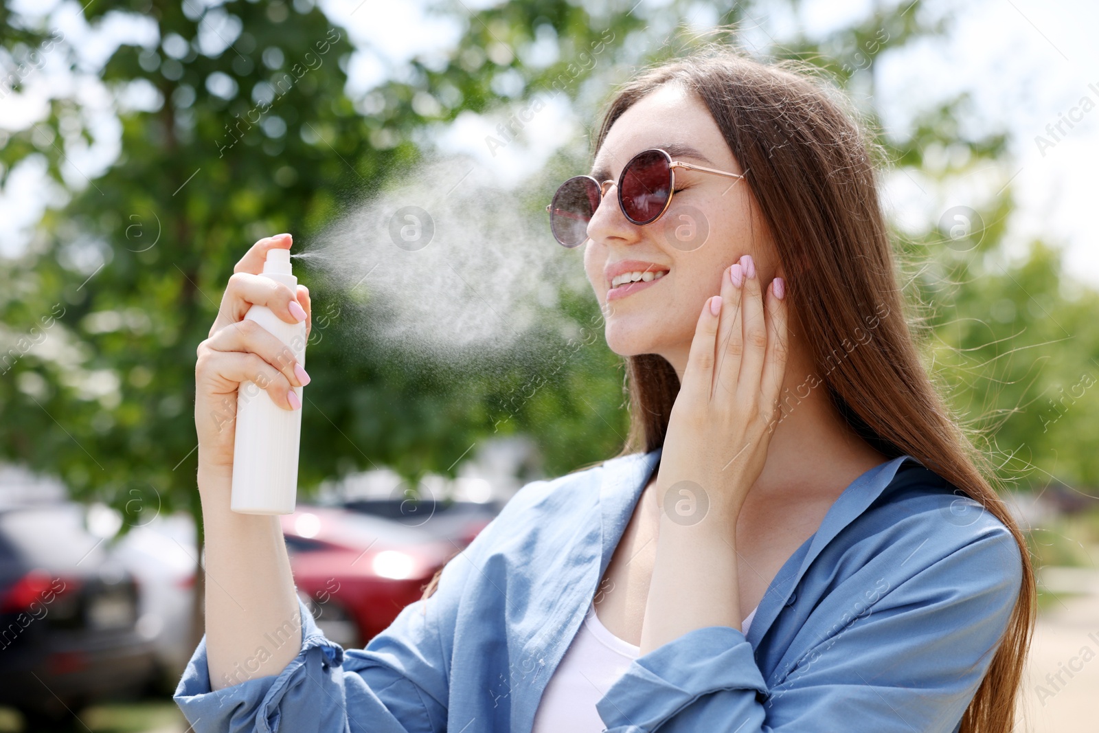 Smiling woman in sunglasses spraying thermal water onto her face outdoors Photo of Smiling woman in sunglasses spraying thermal water onto her face outdoors