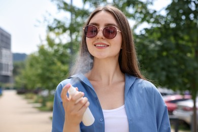 Photo of Smiling woman in sunglasses spraying thermal water outdoors