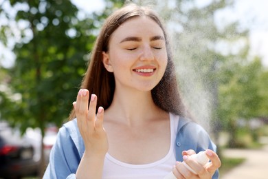 Photo of Smiling woman spraying thermal water from bottle outdoors