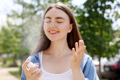 Photo of Smiling woman spraying thermal water from bottle outdoors