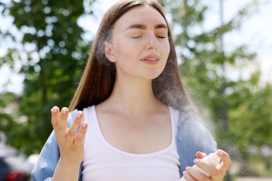 Photo of Beautiful woman spraying thermal water from bottle outdoors