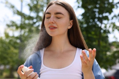 Photo of Beautiful woman spraying thermal water from bottle outdoors