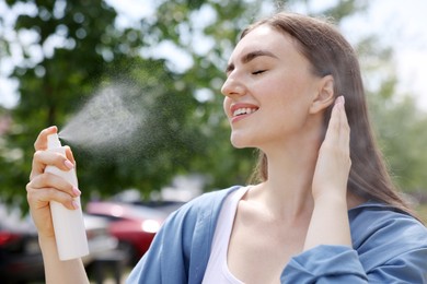 Photo of Smiling woman spraying thermal water onto her face outdoors