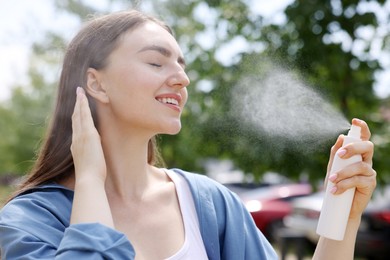 Photo of Smiling woman spraying thermal water onto her face outdoors