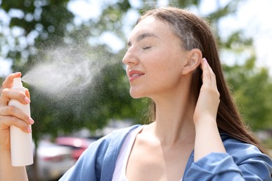 Photo of Smiling woman spraying thermal water onto her face outdoors