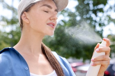 Photo of Beautiful woman in baseball hat spraying thermal water onto her face outdoors