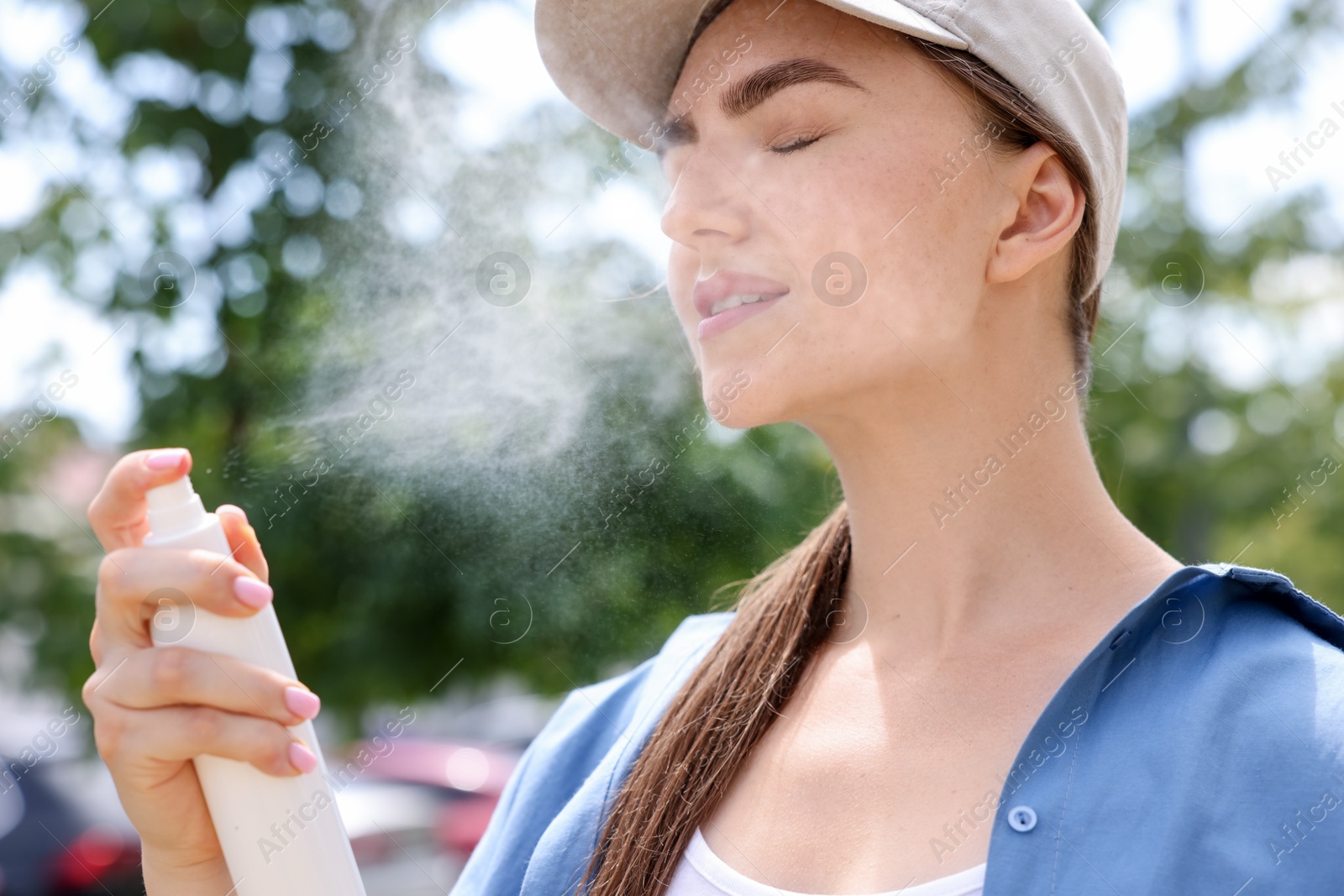 Beautiful woman in baseball hat spraying thermal water onto her face outdoors Photo of Beautiful woman in baseball hat spraying thermal water onto her face outdoors