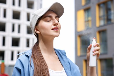 Photo of Smiling woman in baseball hat spraying thermal water outdoors