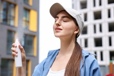 Photo of Smiling woman in baseball hat spraying thermal water outdoors