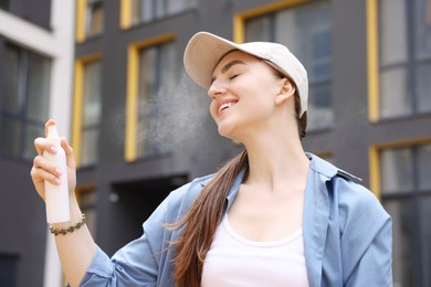 Photo of Smiling woman in baseball hat spraying thermal water onto her face outdoors