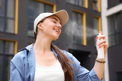 Photo of Smiling woman in baseball hat spraying thermal water onto her face outdoors
