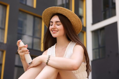 Photo of Smiling woman in straw hat spraying thermal water onto her face outdoors