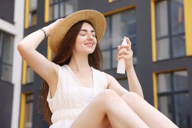 Photo of Smiling woman in straw hat spraying thermal water onto her face outdoors