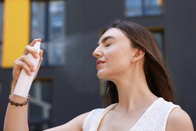 Photo of Beautiful woman spraying thermal water onto her face outdoors