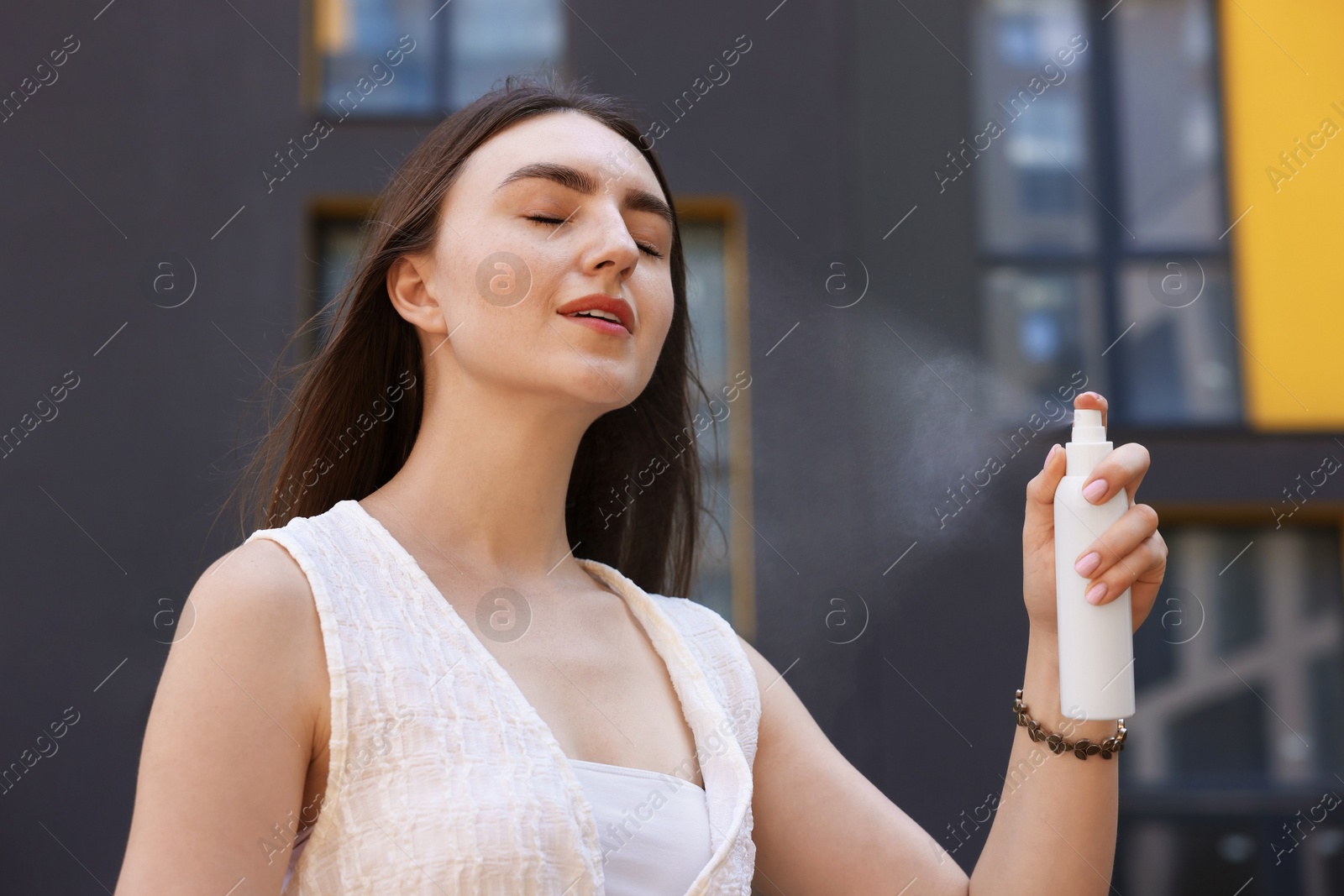 Smiling woman spraying thermal water from bottle outdoors Photo of Smiling woman spraying thermal water from bottle outdoors