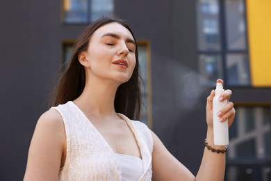 Photo of Smiling woman spraying thermal water from bottle outdoors