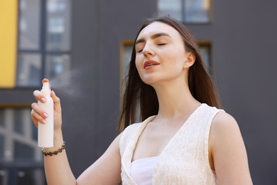 Photo of Beautiful woman spraying thermal water onto her face outdoors
