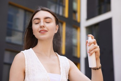 Photo of Smiling woman spraying thermal water from bottle outdoors