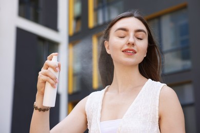 Photo of Smiling woman spraying thermal water from bottle outdoors