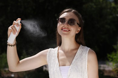Photo of Smiling woman in sunglasses spraying thermal water outdoors