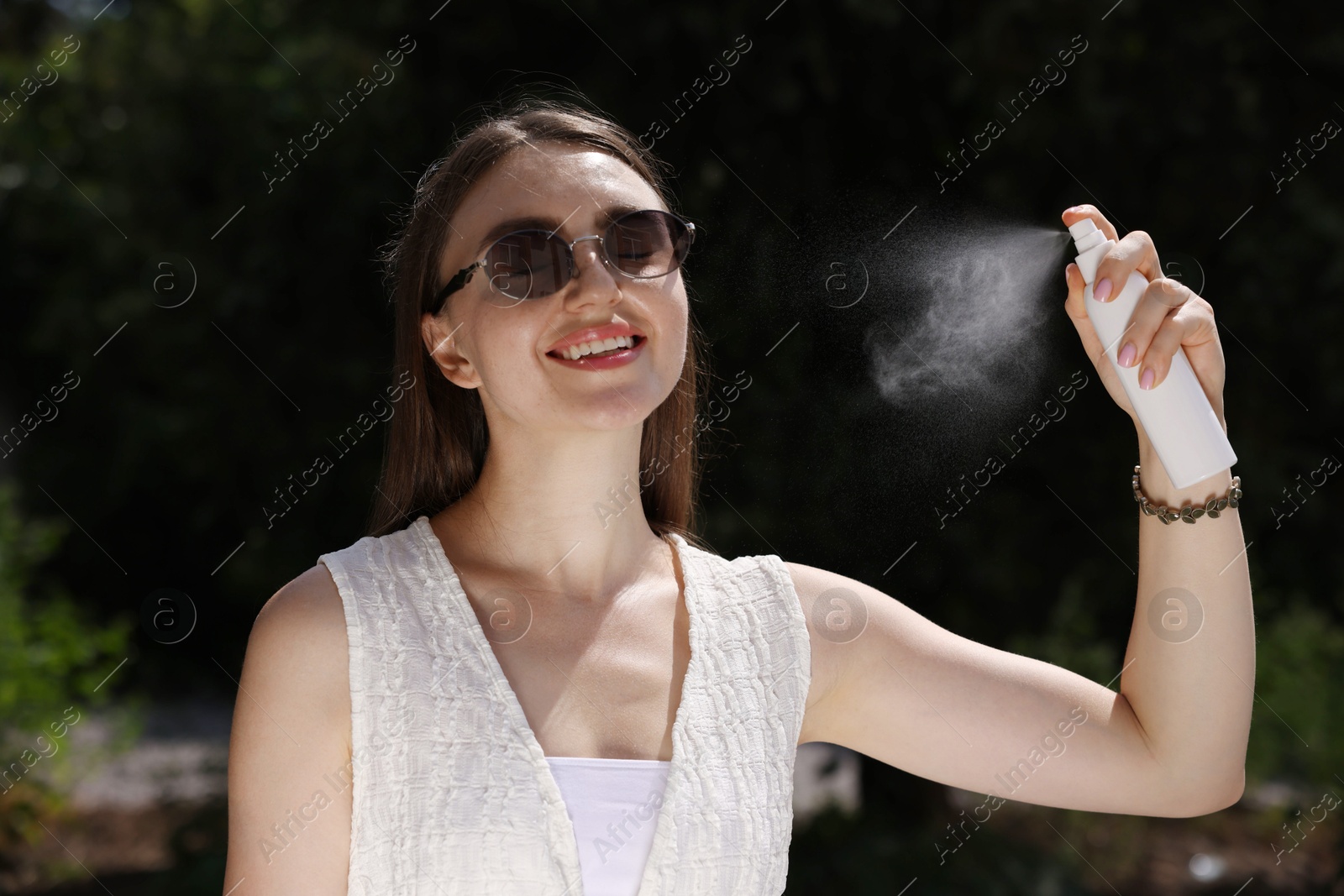 Smiling woman in sunglasses spraying thermal water outdoors Photo of Smiling woman in sunglasses spraying thermal water outdoors