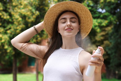 Photo of Smiling woman in straw hat spraying thermal water onto her face outdoors