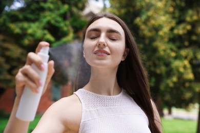 Photo of Smiling woman spraying thermal water from bottle outdoors