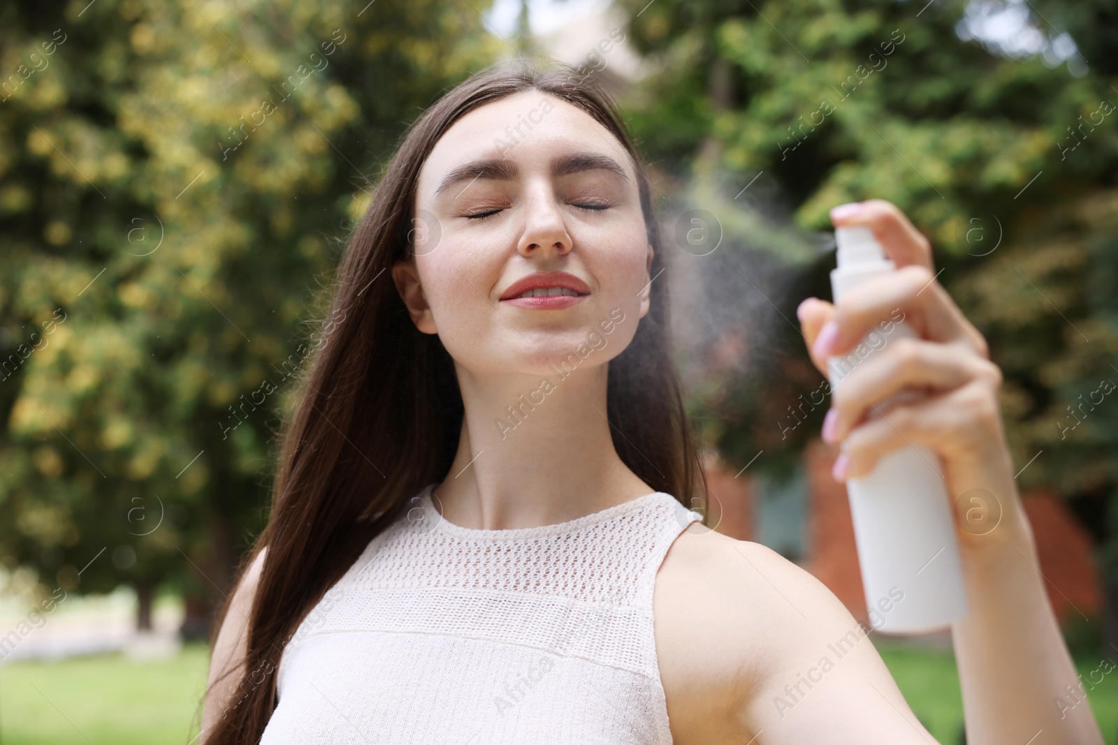 Smiling woman spraying thermal water from bottle outdoors Photo of Smiling woman spraying thermal water from bottle outdoors