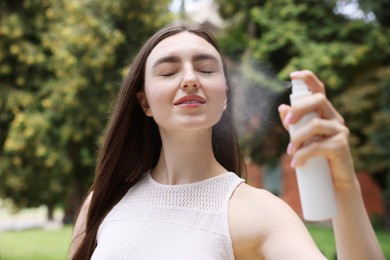 Photo of Smiling woman spraying thermal water from bottle outdoors