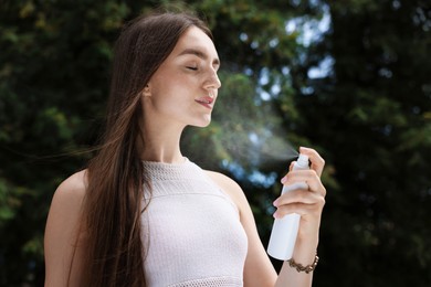 Photo of Smiling woman spraying thermal water from bottle outdoors