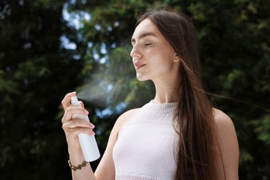 Photo of Smiling woman spraying thermal water from bottle outdoors