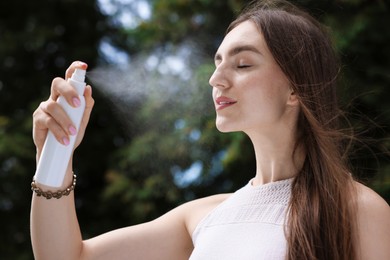 Photo of Smiling woman spraying thermal water onto her face outdoors