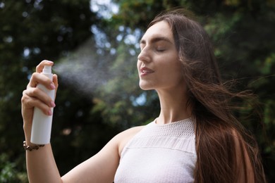 Photo of Smiling woman spraying thermal water onto her face outdoors
