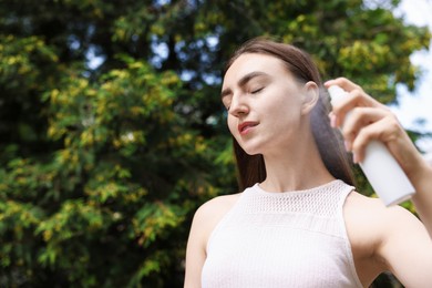 Photo of Smiling woman spraying thermal water onto her face outdoors. Space for text