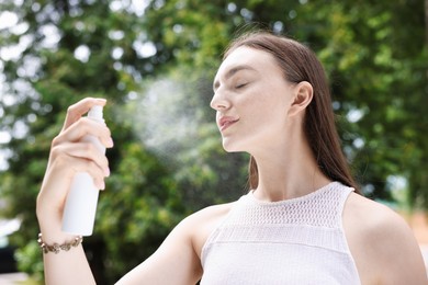 Photo of Smiling woman spraying thermal water onto her face outdoors