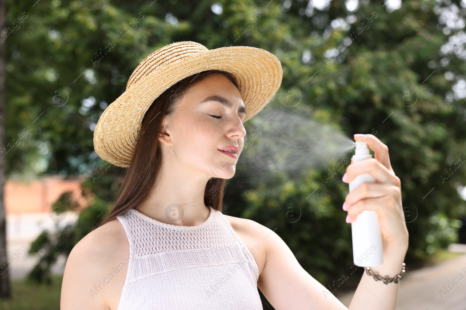 Smiling woman in straw hat spraying thermal water onto her face outdoors Photo of Smiling woman in straw hat spraying thermal water onto her face outdoors