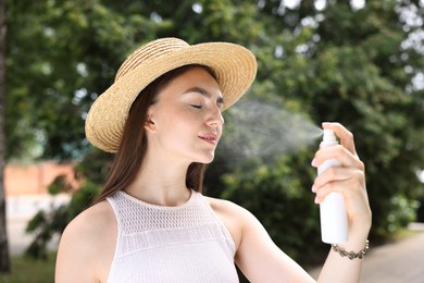 Photo of Smiling woman in straw hat spraying thermal water onto her face outdoors