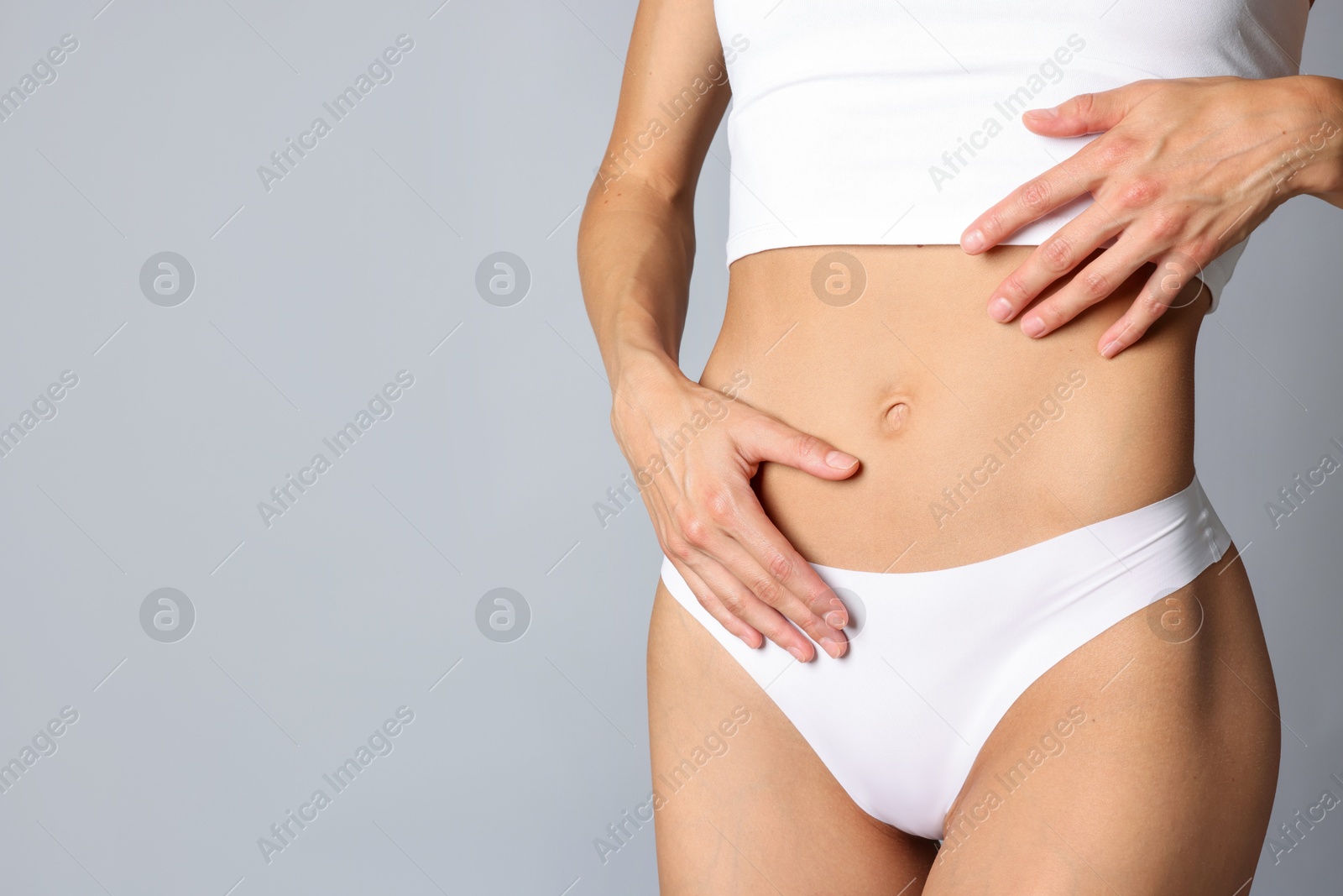 Woman with flat belly on grey background, closeup. Space for text Photo of Woman with flat belly on grey background, closeup. Space for text