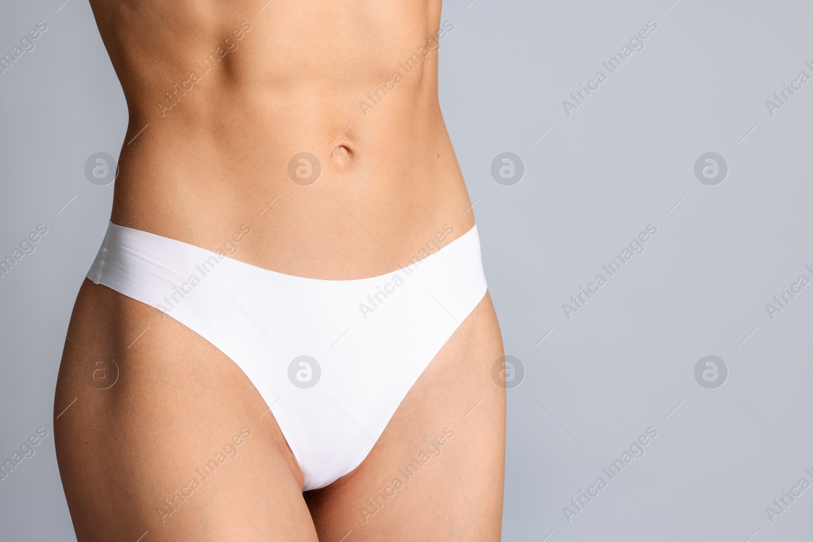 Woman with flat belly on grey background, closeup. Space for text Photo of Woman with flat belly on grey background, closeup. Space for text