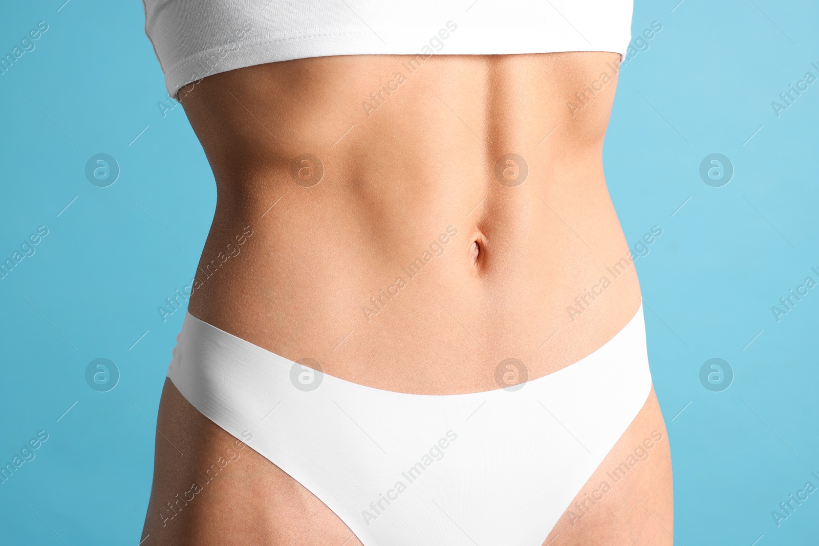 Woman with flat belly on light blue background, closeup Photo of Woman with flat belly on light blue background, closeup