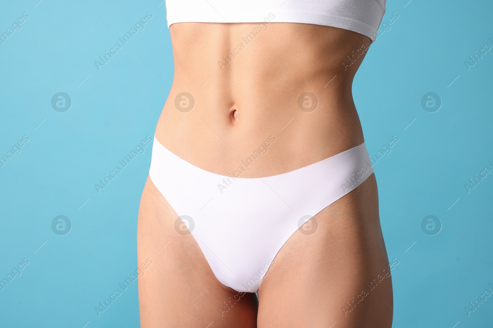 Woman with flat belly on light blue background, closeup Photo of Woman with flat belly on light blue background, closeup