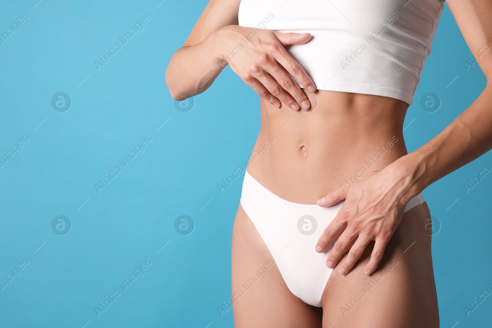 Woman with flat belly on light blue background, closeup. Space for text Photo of Woman with flat belly on light blue background, closeup. Space for text