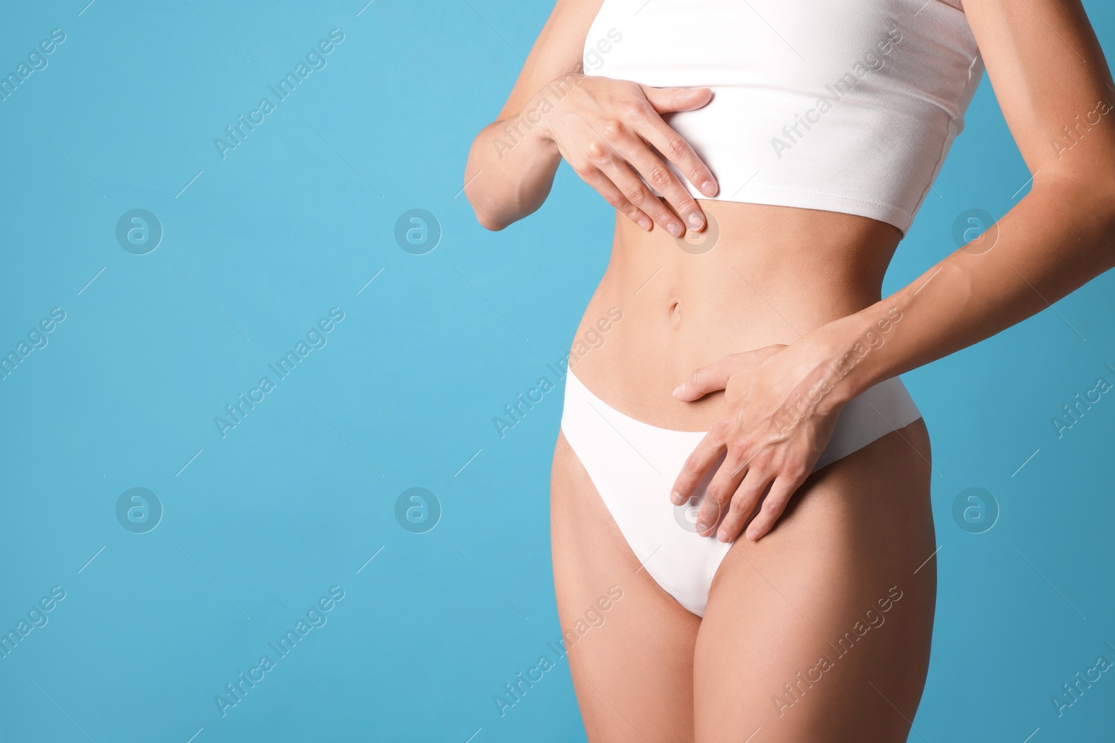 Woman with flat belly on light blue background, closeup. Space for text Photo of Woman with flat belly on light blue background, closeup. Space for text