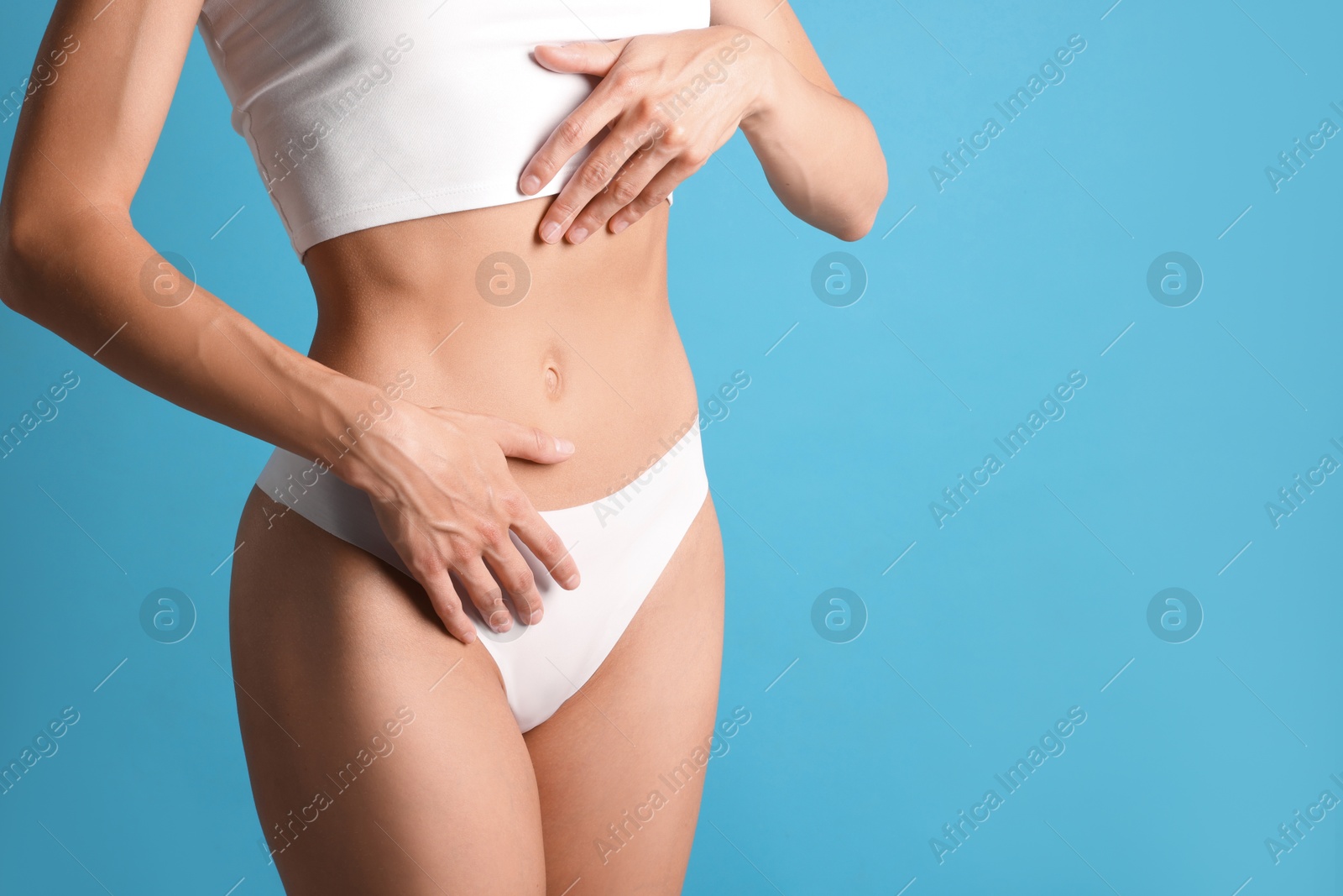 Woman with flat belly on light blue background, closeup. Space for text Photo of Woman with flat belly on light blue background, closeup. Space for text