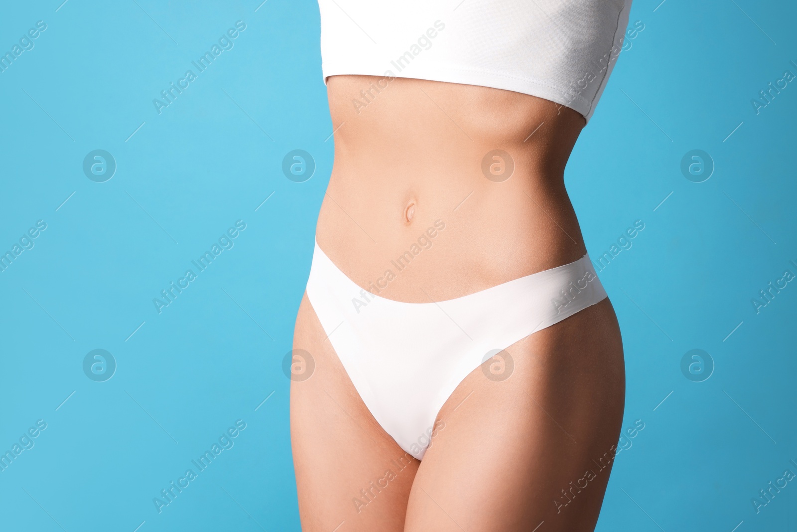 Woman with flat belly on light blue background, closeup. Space for text Photo of Woman with flat belly on light blue background, closeup. Space for text
