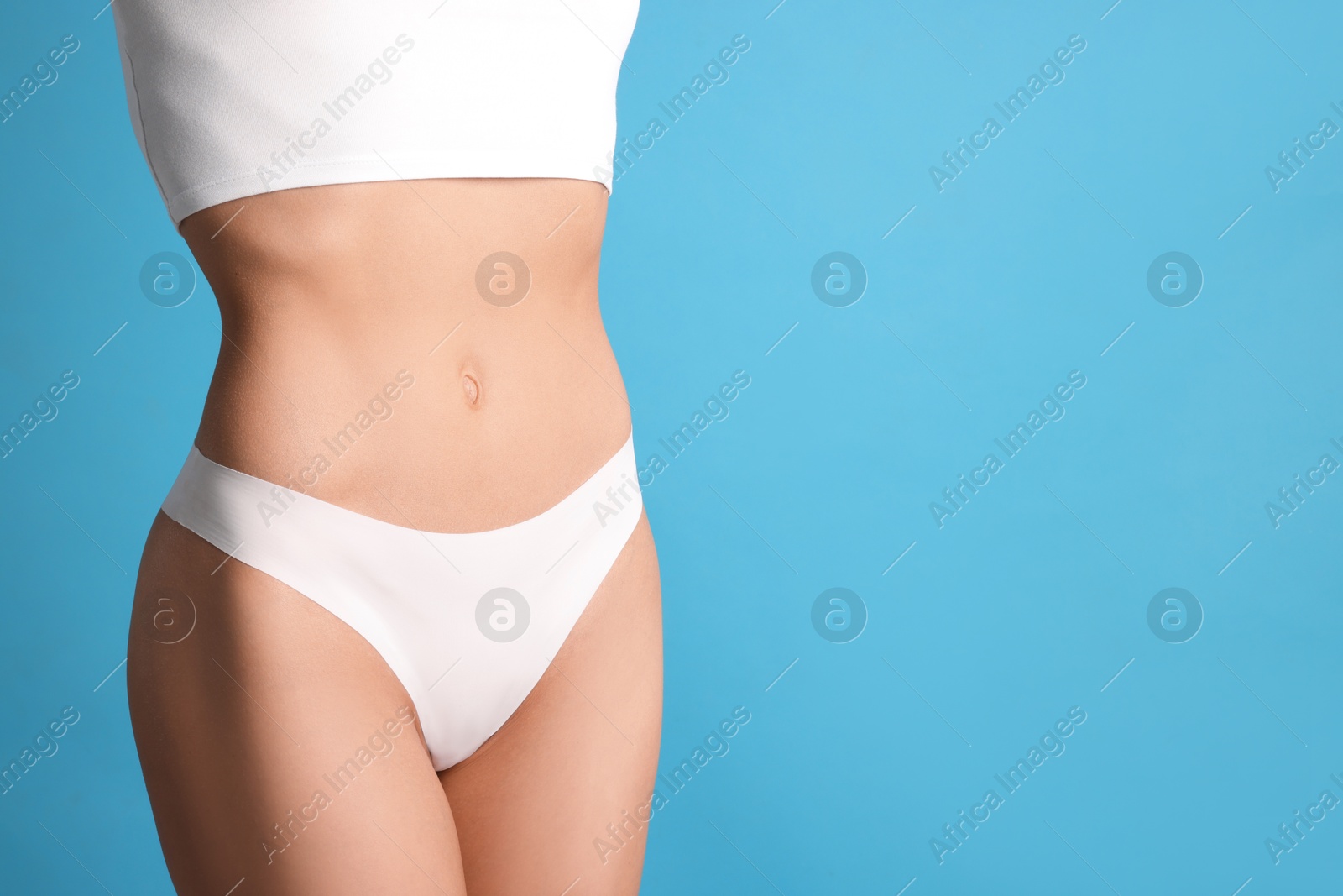 Woman with flat belly on light blue background, closeup. Space for text Photo of Woman with flat belly on light blue background, closeup. Space for text
