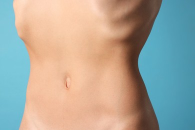 Photo of Woman with flat belly on light blue background, closeup
