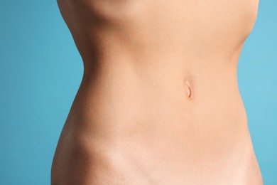 Photo of Woman with flat belly on light blue background, closeup